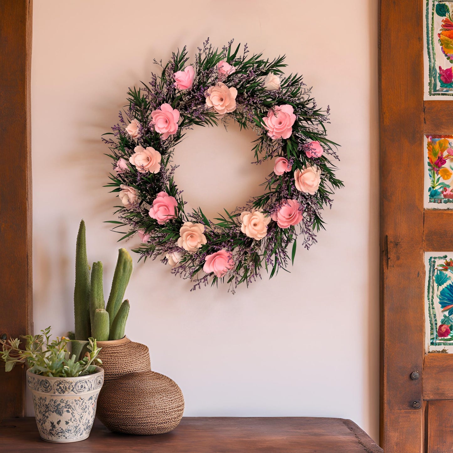 Floral wreath with pink flowers on a wall next to potted plants and wooden door