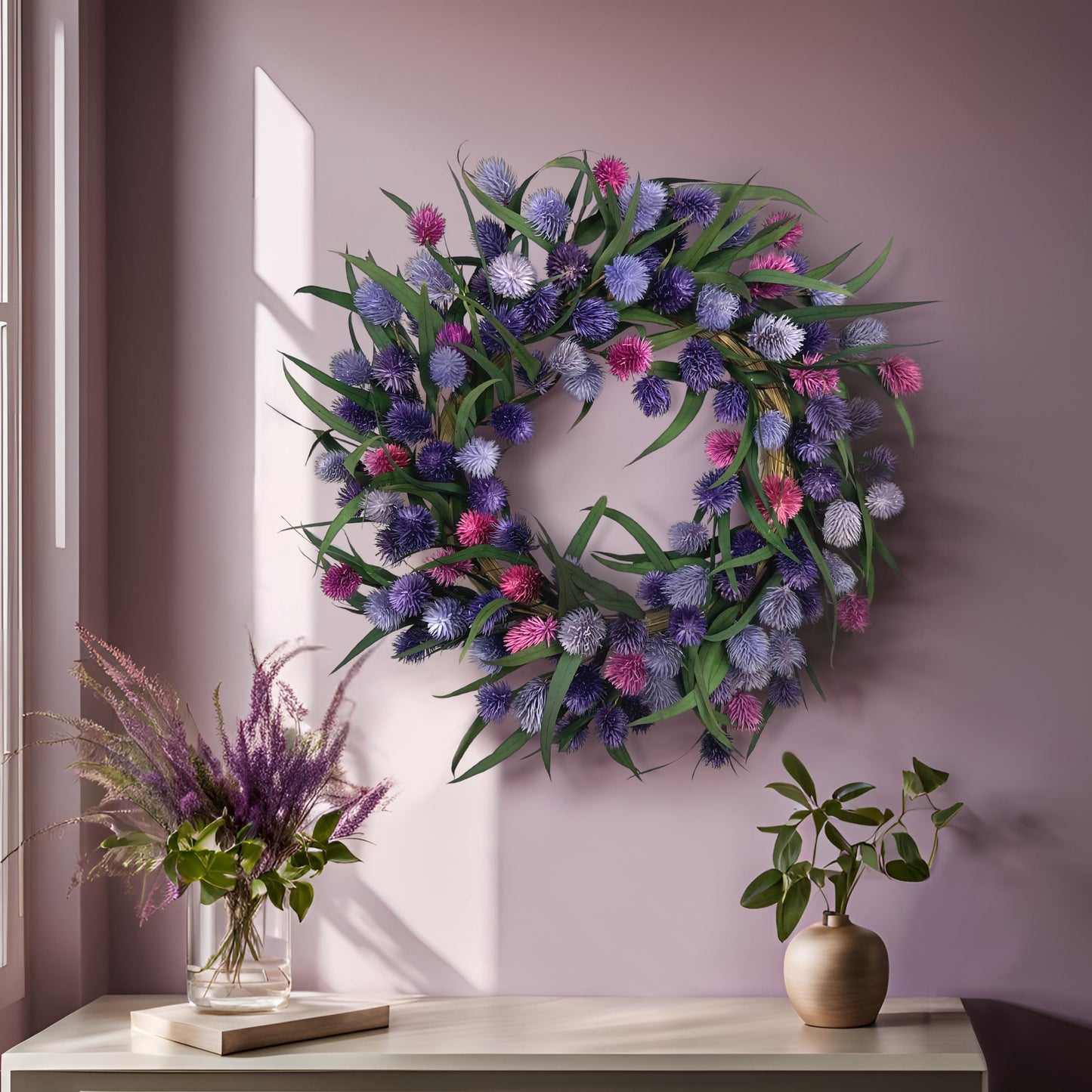 preserved eucalyptus wreath with purple platycarya balls on a pink wall on top of a white table with blooms and greenery on it