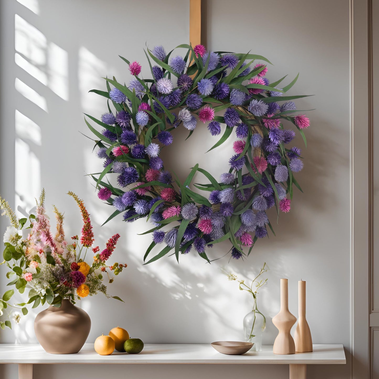 purple preserved spring wreath on a white wall on top of a mantle with flowers and candle holders on it