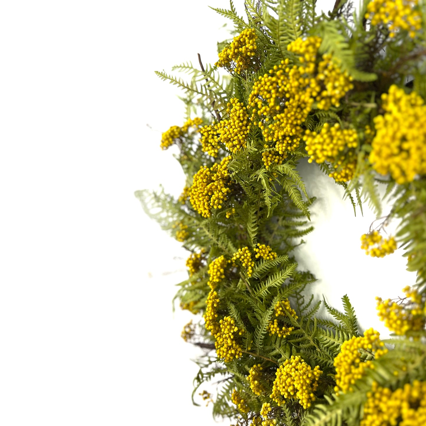 a side view of the yellow rice flower and fern wreath on a white wall