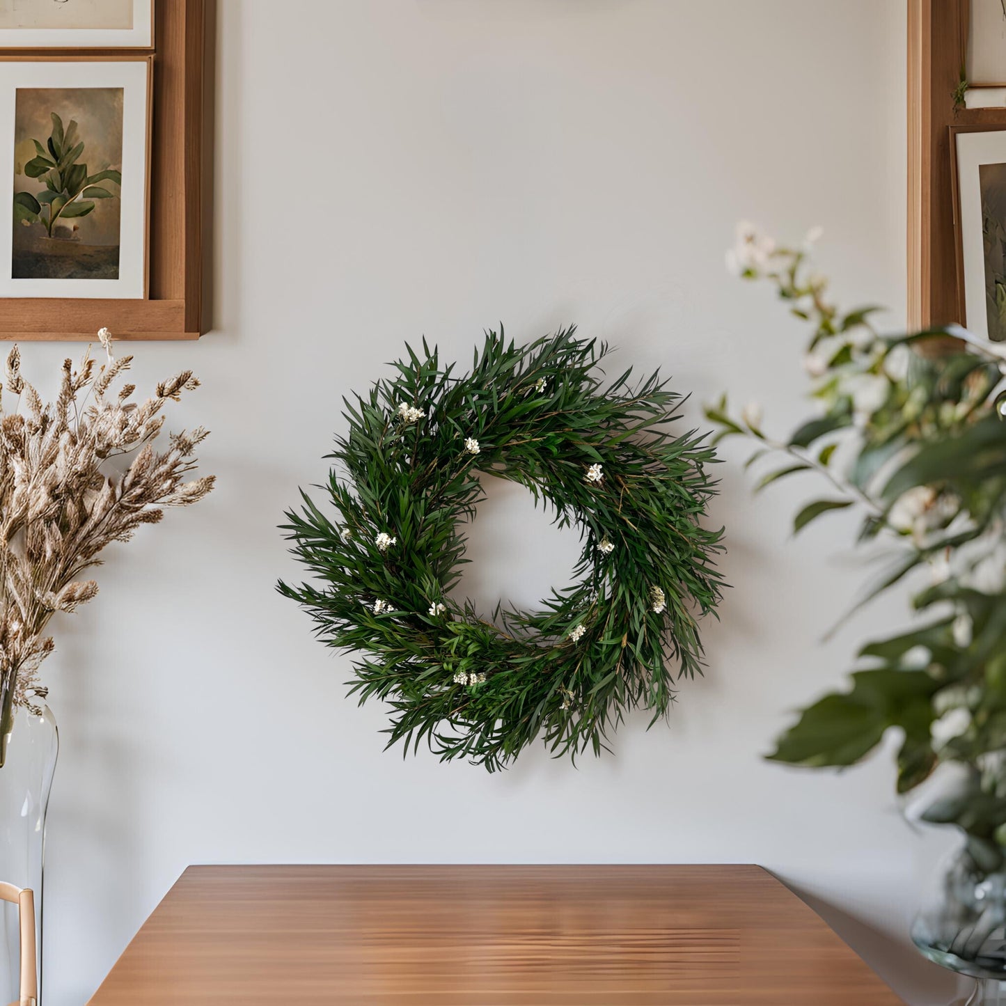 preserved handmade wreath dotted with white daisy flowers on top of a wooden table with fall greeneries around