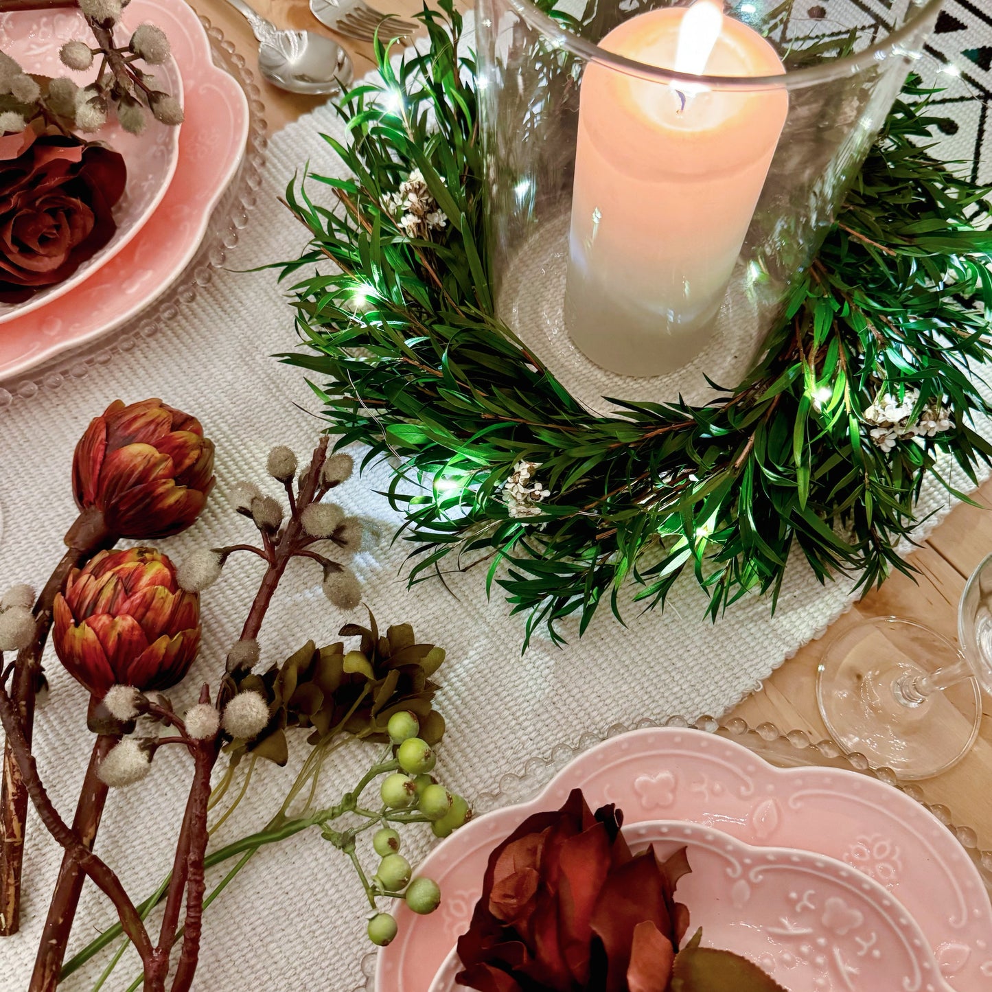 Cozy Christmas tablescape with lit candle centerpiece in a preserved foliage wreath and floral accents