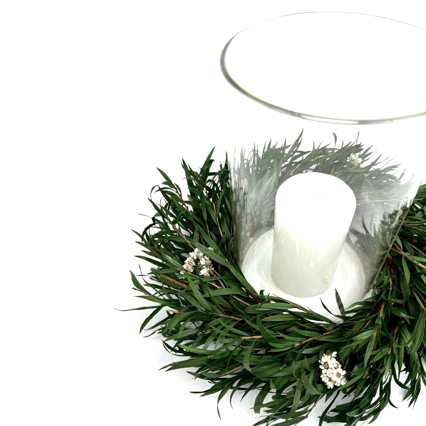Small preserved greenery candle ring wreath with white daisies, surrounding a glass hurricane holder and white pillar candle
