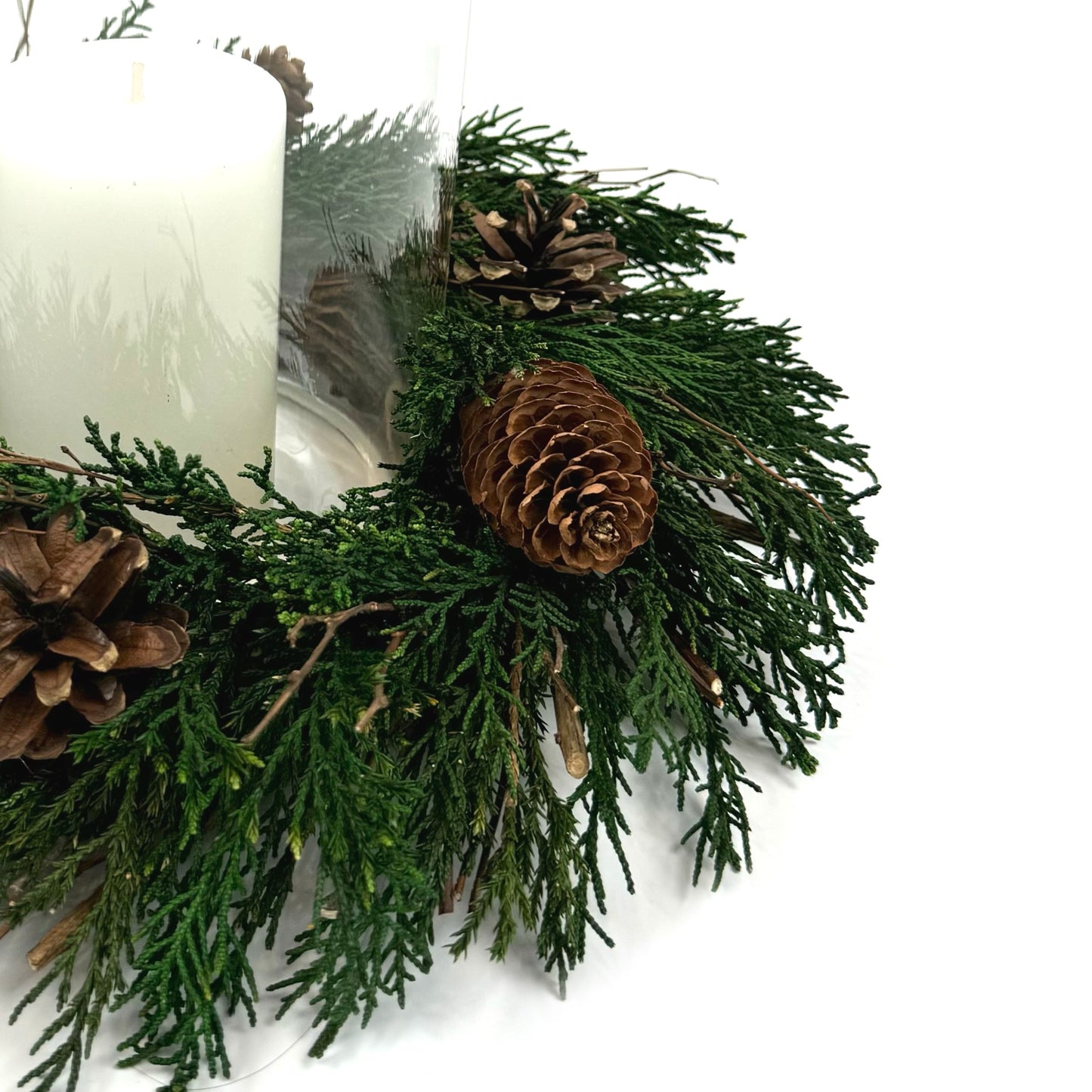 closeup look of christmas candle ring wreath with pinecones and juniper leaves