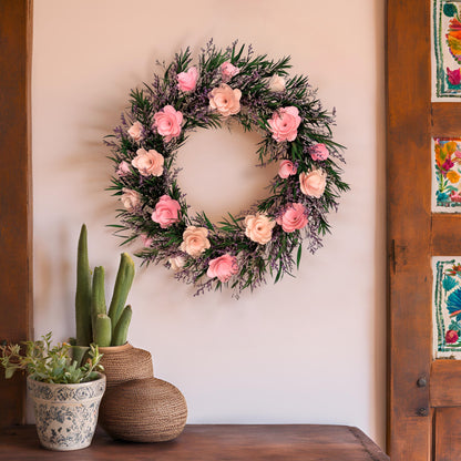 Floral wreath with pink flowers on a wall next to potted plants and wooden door