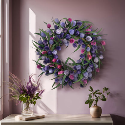 preserved eucalyptus wreath with purple platycarya balls on a pink wall on top of a white table with blooms and greenery on it