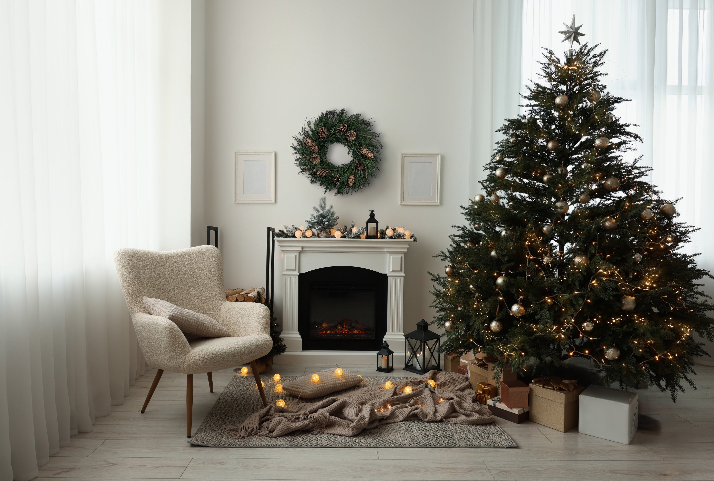 a cozy festive white living room with a big christmas tree to the right, a white fireplace and a preserved pinecone wreath in the middle, and a off-white accent chair to the left. Decorated with lots of string lights and gift boxes on the floor